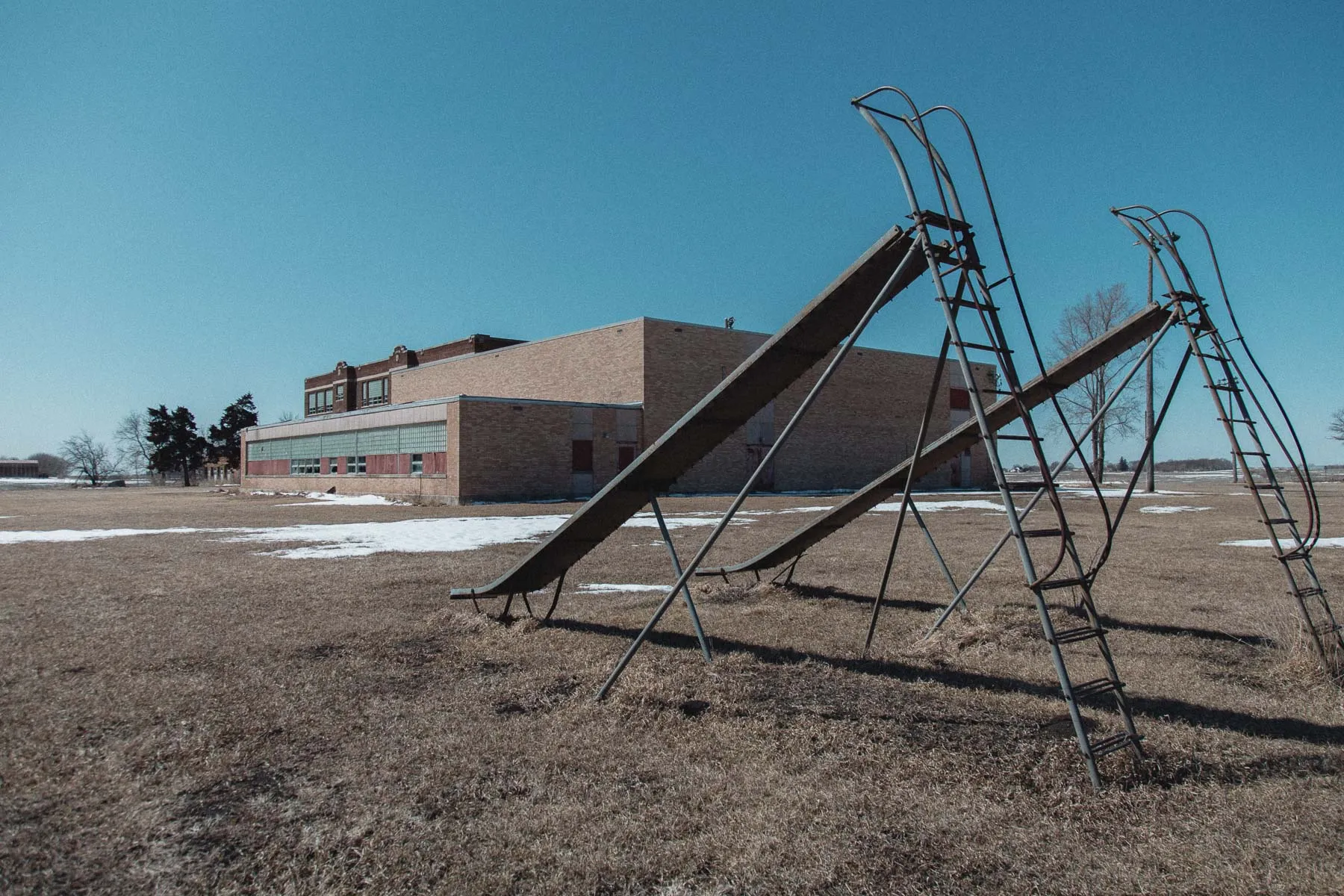 Rusting metal playground slides behind Ayrshire Consolidated School